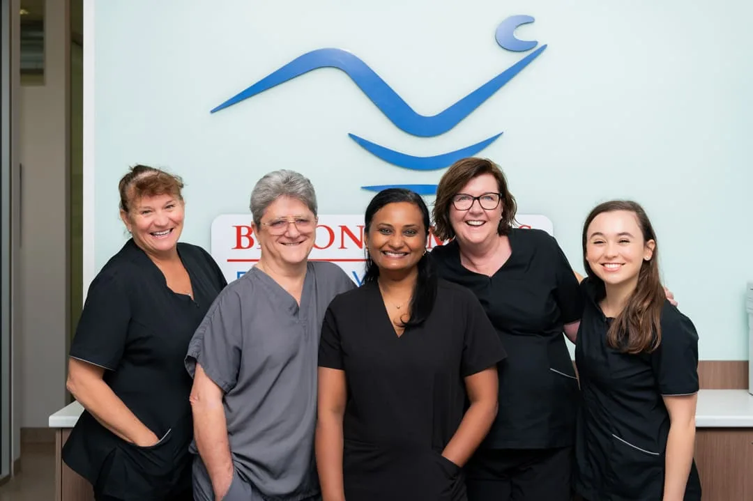 The team at Beyond Smiles Family Dental &mdash; five staff members before the practice's blue-wave logo wall.